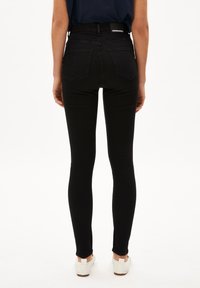 Vaqueros negros skinny de talle alto con bolsillos traseros. Hechos de denim elástico, presentan una cinturilla sin costuras y un ajuste slim que llega hasta el tobillo.