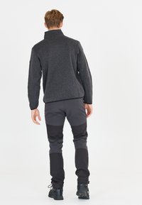 Pólder de forro polar negro con cuello alto, combinado con pantalones ajustados en bloques de color gris y negro, y botas de exterior negras.