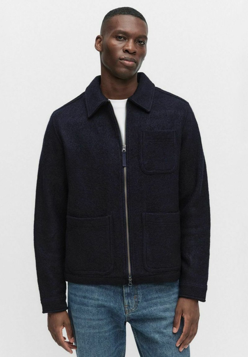 Takkaharmaa villatakki, jossa on vetoketju, kaksi etutaskua ja kaulus. Rentomallinen, tekstiililtä tekstuuri. Yhdistetty vaaleansiniisiin farkkuihin.