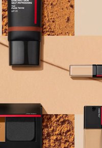 Envases cosméticos negros y transparentes: un líquido tintado con tapa negra y acento rojo, un corrector transparente y un compacto negro con un interior dorado y negro.