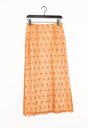 Jupe midi orange avec superposition en dentelle florale et petits sequins, suspendue sur un cintre noir contre un fond blanc.