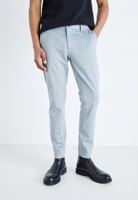 Jasnoszare spodnie typu tailored z teksturowanej tkaniny, z kieszeniami z przodu i slim fit, połączone z czarnymi skórzanymi botkami za kostkę.
