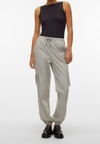 Pantalons cargo gris clair avec des poignets élastiques et une taille ajustable, dotés de poches latérales et d'un matériau lisse et léger. Débardeur noir.