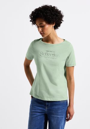 Light green short-sleeve shirt with a rounded neckline, featuring a reflective text design on the front. Paired with blue jeans.