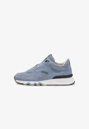 Zapatilla de ante gris con parte superior texturizada, detalles contrastantes en negro y suela blanca con diseño de zigzag. Presenta cordones tradicionales y detalle de marca.