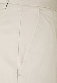 Pantalon en coton beige avec une texture lisse, doté d'une poche latérale et de détails de coutures subtiles sur les coutures.