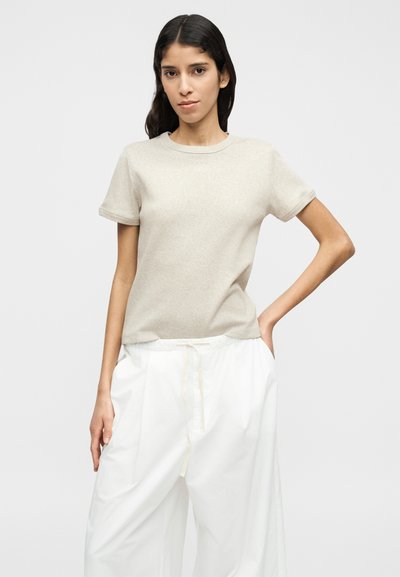 Μπεζ βαμβακερό μπλουζάκι με κοντά γυριστά μανίκια, λαιμόκοψη στρόγγυλη και άνετη εφαρμογή, συνδυασμένο με λευκό, φαρδύ παντελόνι. Απλό σχέδιο, χωρίς σχέδια.