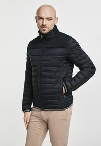 Czarna kurtka puchowa z wysokim kołnierzem, z poziomą pikowaną teksturą, kieszeniami na zamek oraz kontrastowymi paskami u dołu i przy mankietach.