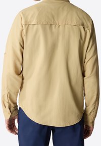 Camicia a maniche lunghe giallo chiaro con orlo curvo, polsini con bottoni e dettaglio a ventaglio sul retro, realizzata in un tessuto leggero.
