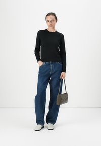 Svart langermet genser, løse blå jeans, hvite sko, og en liten brun veske med zigzag-mønster. En enkel, uformell antrekk.