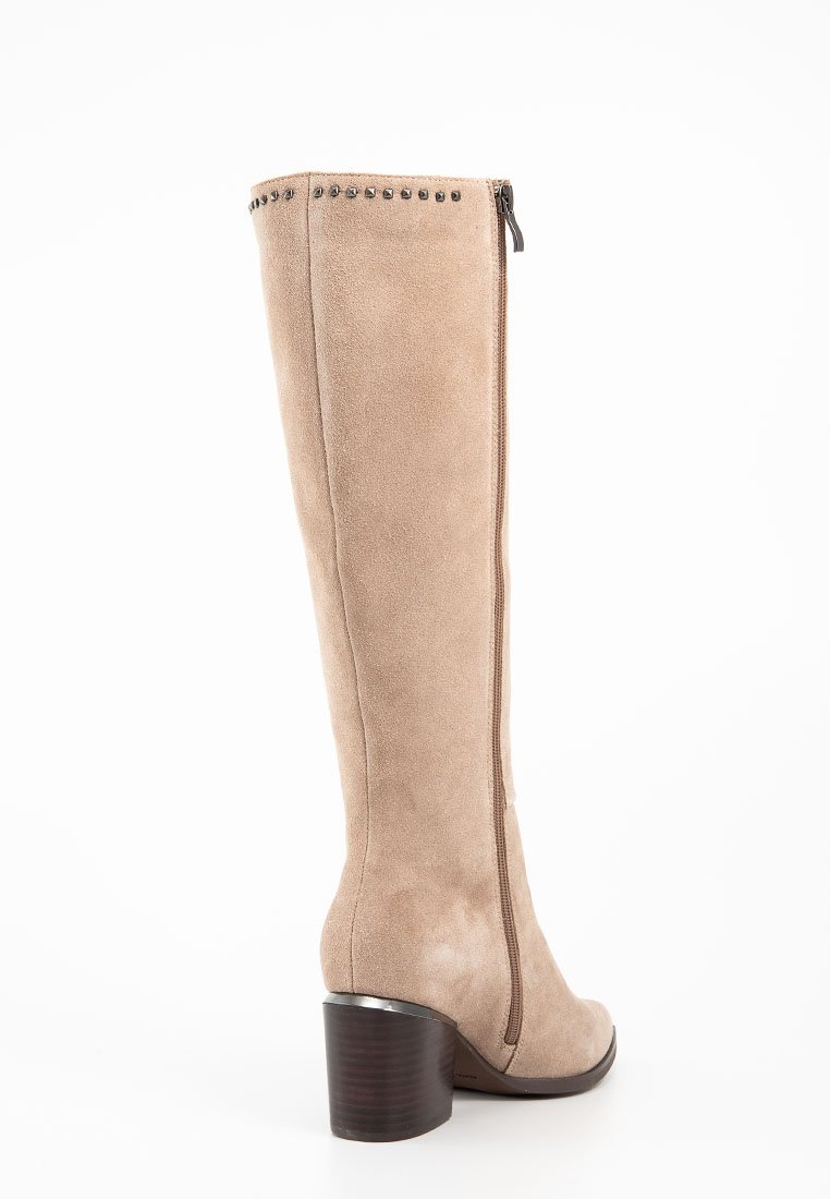 Bota de ante beige hasta la rodilla con cremalleras laterales, acento plateado en el tacón y detalles de tachuelas a lo largo del borde superior. Tacón de madera grueso.