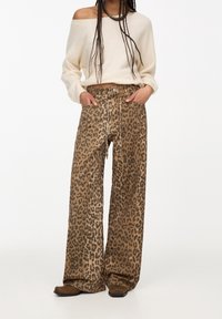 Pantalon à jambes larges avec imprimé léopard, présentant un schéma de couleurs marron et beige, une taille à cordon de serrage et une texture de tissu douce.