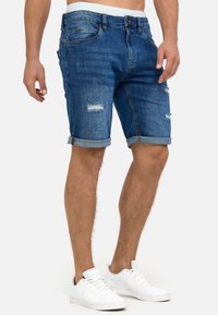 Shorts en denim dans un délavé bleu moyen avec des détails usés et des ourlets retroussés. Fabriqués en mélange de coton, dotés de cinq poches.