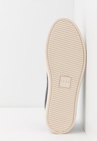 Black sneaker sole with beige rubber outsole. Features horizontal ridges, logo imprint, and curved edges for improved traction.