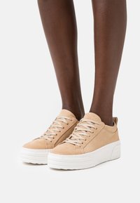Sapatilhas de camurça bege com biqueira redonda, design com atacadores, sola plataforma branca e estilo minimalista. Parte superior texturizada com detalhes cosidos.