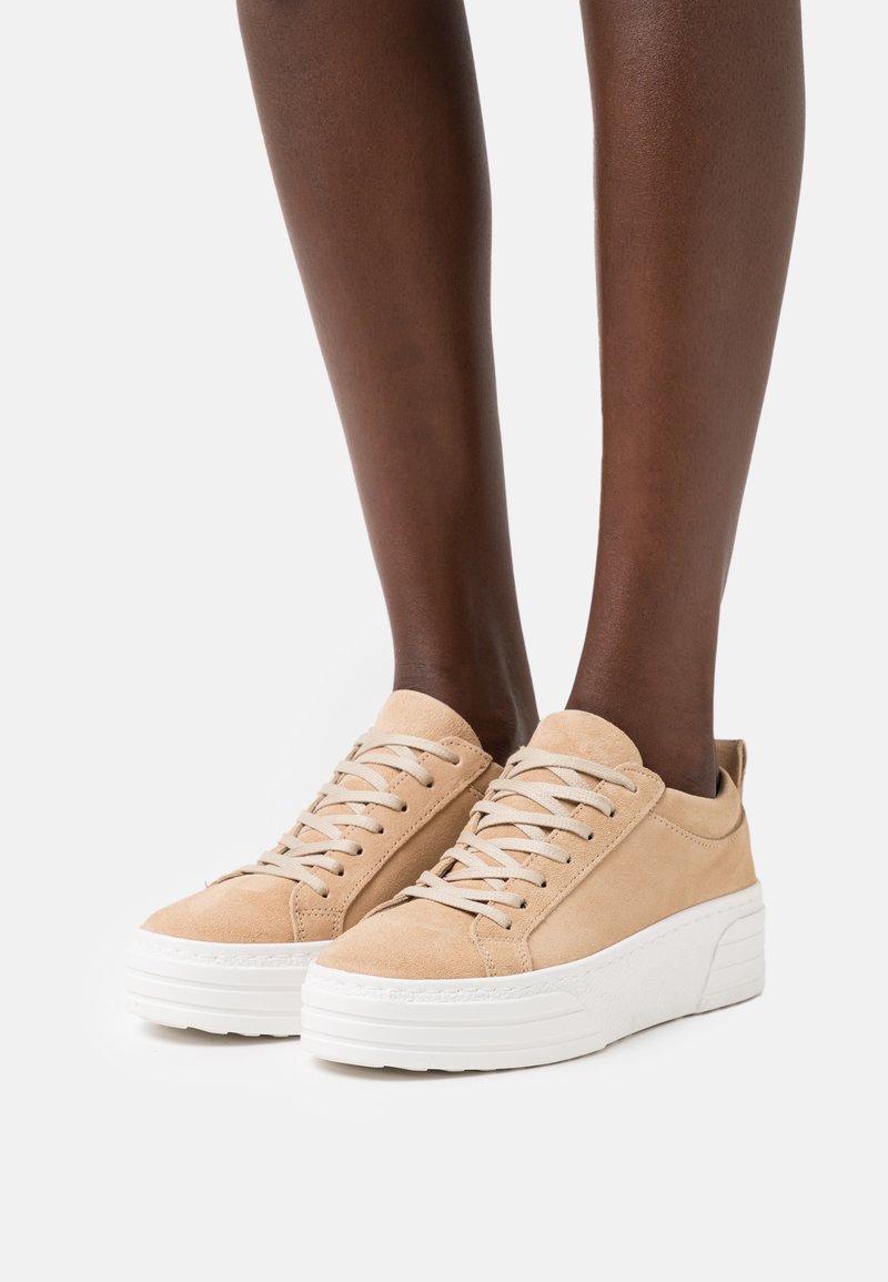Sapatilhas de camurça bege com biqueira redonda, design com atacadores, sola plataforma branca e estilo minimalista. Parte superior texturizada com detalhes cosidos.