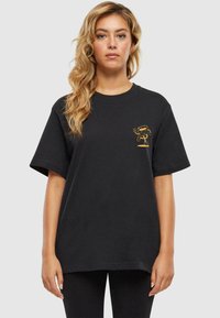 Schwarzes Baumwoll-T-Shirt mit kurzen Ärmeln, das ein kleines gelbes Grafikdesign auf der Brust zeigt. Entspannter Schnitt und weiche Textur.