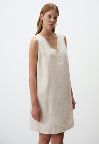 Leinen A-Linien-Kleid in Hellbeige mit V-Ausschnitt und ohne Ärmel. Glatte Textur, knielang und minimalistisches Design.