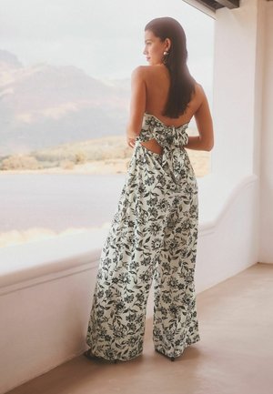 Lillekangast lillemustriga jumpsuit, millel on laiad säärted, avatud selg ja paeltega detail vööl. Värvideks on valge ja must.