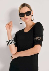 Black short-sleeve top with lace detailing, paired with oversized black sunglasses and bold black-and-white patterned bracelets.