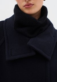 Navy uldfrakke med store klapkraver og en sort ribstrik krave. Glat tekstur med synlige stikninger.