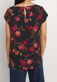 Blommig blus med mörk bakgrund, kort ärm och en liten nyckelhålöppning på baksidan, med röda och rosa blommönster.