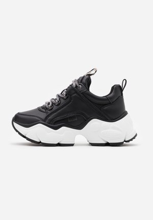 Czarny skórzany sneaker z masywną białą podeszwą, grubymi czarno-białymi sznurowadłami oraz pętlami do zakładania na języku i pięcie, pokazany z profilu.