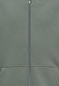 Sudadera verde con cremallera central plateada y bolsillos frontales, mostrando un detallado de la textura del tejido y las costuras.