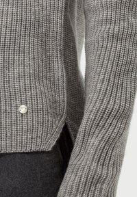 Pull gris en maille avec texture côtelée, orné d'un détail perlé à l'ourlet. Présente une coupe décontractée et des fentes latérales pour faciliter les mouvements.