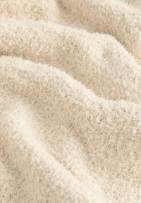 Krémová látka s plyšovým, texturovaným povrchem, která má měkké, vyvýšené vlákna vytvářející útulný a teplý vzhled.