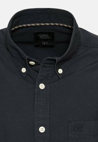 Donker marineblauw overhemd met knopen van katoen. Het shirt heeft een kraag, witte knopen, een borstzak en een klein logo op de zak.