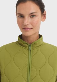 Groene gewatteerde jas met een hoge kraag, volledige rits en golvende patronen op de stof, die een gladde en gestructureerde uitstraling biedt.