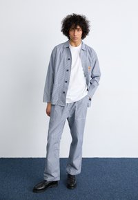Blue and white striped two-piece outfit with a button-up jacket and matching pants, made of lightweight fabric, worn with a white shirt and black shoes.