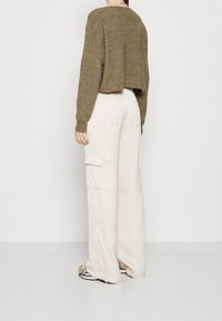 Pull court vert olive en tissu texturé, associé à un pantalon cargo large couleur crème avec poches latérales et coupe décontractée.