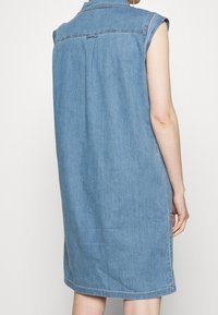 Abito in denim senza maniche di colore blu chiaro, con colletto, taglio dritto e spacchi laterali con dettagli di cucitura visibili.