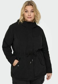 Juodas džemperis su virvute juosmenyje, gobtuvu ir šoninėmis kišenėmis. Minkšta, tekstūruota medžiaga su mygtukų ir užtrauktuko uždarymu, užtikrinančiu funkcionalumą.