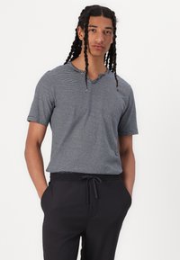 Grå kortermet t-skjorte med horisontale striper, V-halsdesign og myk tekstur, brukt sammen med svarte joggebukser med snor.