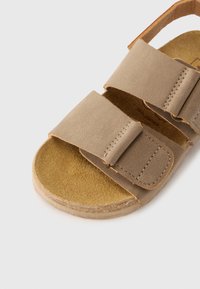 Ανοιχτό καφέ σανδάλι με δύο φαρδιές λουρίδες και απαλή σουέντ υφή. Διαθέτει μαξιλαρωτό εσωτερικό πέλμα και στρογγυλεμένη ελαστική σόλα.