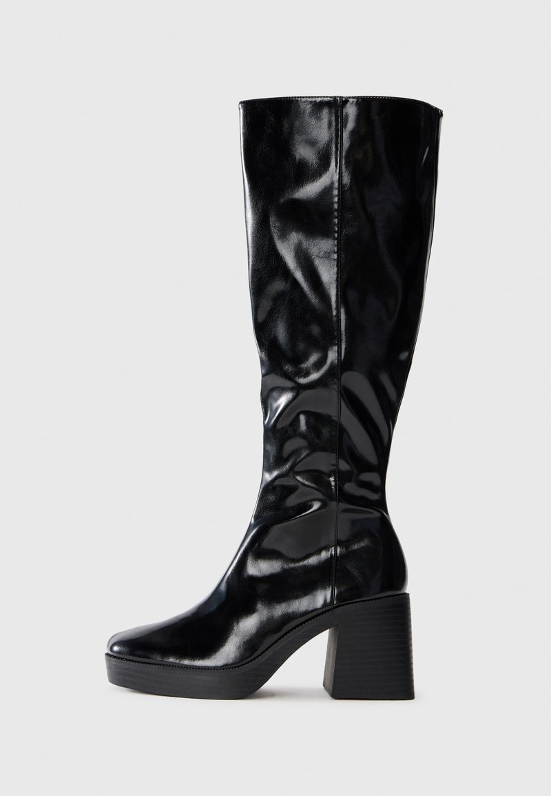 Black, knee-high boot made from shiny patent leather; features a structured block heel and rounded toe. Simplistic, sleek design.