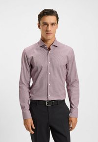 Chemise à manches longues à carreaux dans des tons de violet clair et blanc, en tissu, dotée d'un col classique et d'un devant à boutons. Portée avec un pantalon noir.