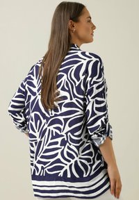 Navy blauwe en witte lange mouwen shirt met een bladerenpatroon, zachte textuurstof en opgerolde mouwen met knoopaccenten.