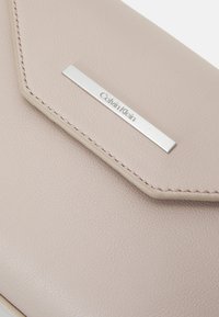 Portfel Calvin Klein w jasnoróżowej skórze o teksturowanym wykończeniu, zdobiony srebrną plakietką z logo oraz tonowaną nicią na krawędzi.