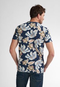 Lyhythihainen tummansininen paita, jossa on suuria kukkakuoseja vaaleissa väreissä, ja vihreitä lehtiä sekä beigejä kukkia, valmistettu pehmeästä ja kevyestä kankaasta.