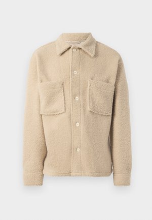 Beige fleece shirt jacket with a pointed collar, front button closure, and two chest pockets. Soft texture with a casual design.