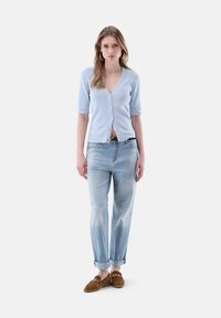 Hellblaues, kurzärmeliges Cardigan mit V-Ausschnitt und Knopfleiste, kombiniert mit hellen, umgeschlagenen Jeans und braunen Wildleder-Leder-Schuhen.