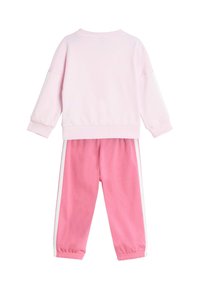 Svetlo ružová mikina s dlhými rukávmi a bielymi pruhmi. Zodpovedajúce ružové tepláky s elastickým pásom a bielymi bočnými akcentmi.