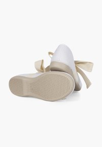 Witte stoffen schoenen met een gestructureerd oppervlak, gebogen neuzen en beige rubberen zolen. Voorzien van een grote beige strik aan de zijkant.