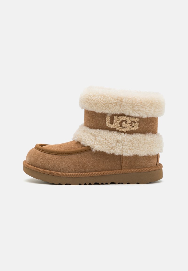 Bottine en daim marron avec un épais revers en shearling crème et logo UGG sur le côté, avec une semelle en caoutchouc plate.