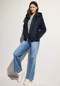 Giacca a piuma blu navy con cappuccio, maglietta a righe sotto, jeans a gamba larga blu chiaro e sneakers bianche. Tessuto liscio, design casual.