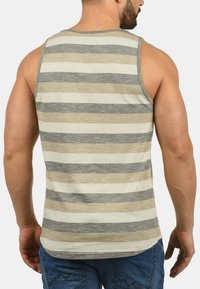 Top de tirantes a rayas en beige, gris y blanco. Presenta un corte relajado y un cuello redondo. La tela parece suave con una textura sutil.